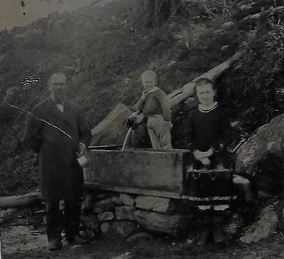 TINTYPE PHOTO #T678  OUTDOORS - FAMILY OF 3 POSING NEXT TO A MOUNTAINSIDE  WELL
